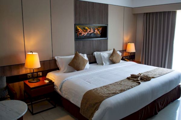 A cozy hotel room features a large bed with pillows, bedside tables with lamps, wall art, and a window with curtains.
