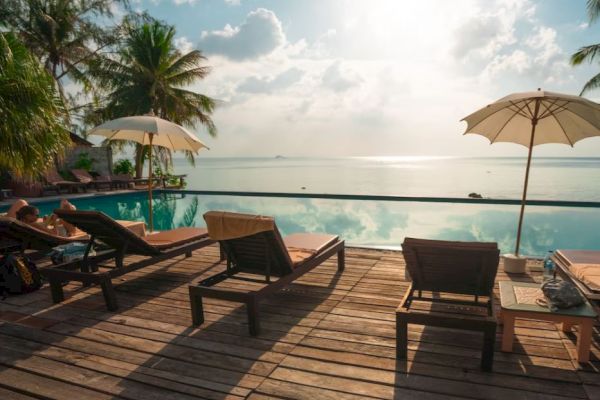 A serene poolside with lounge chairs, umbrellas, and a view of the ocean under a partly cloudy sky.