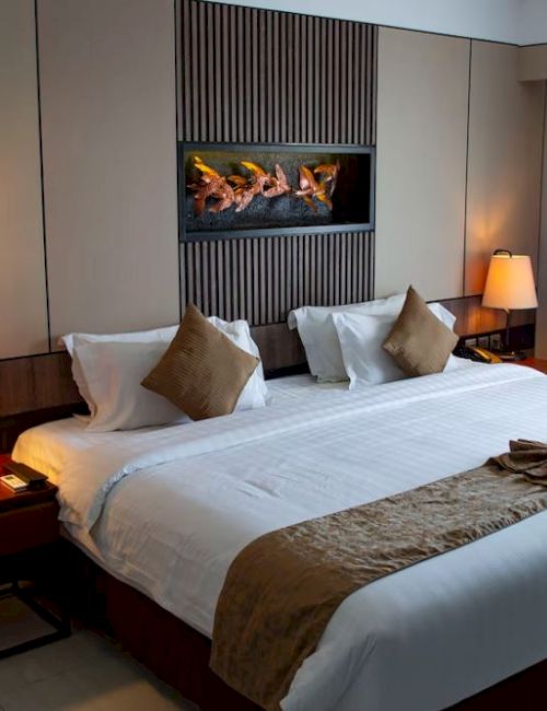 A cozy hotel room with a large bed, decorative pillows, bedside lamps, and a modern wall art piece above the bed.