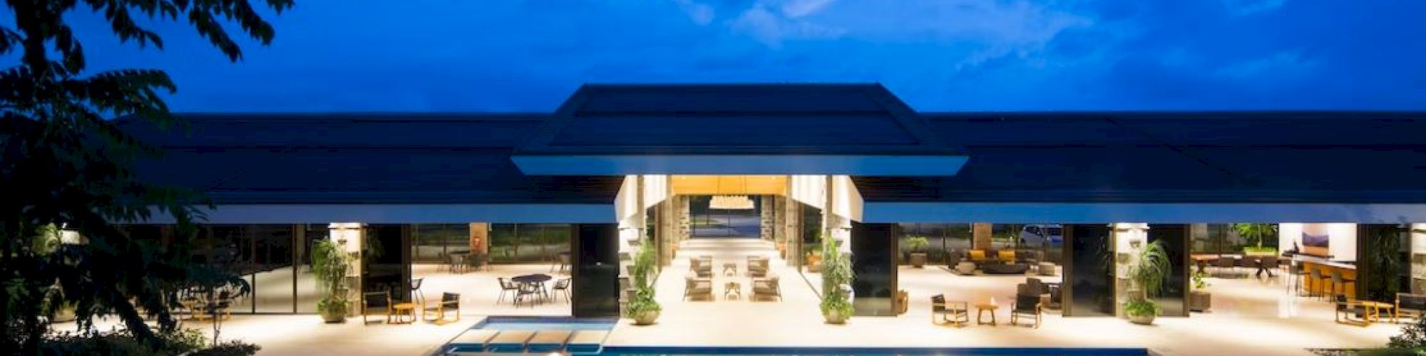 A luxurious building with a glowing pool and lounge area, set against a twilight sky.