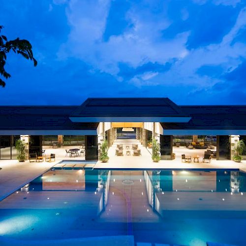 Luxurious pool and modern building at dusk, with illuminated interiors and tranquil surroundings, set against a twilight sky.