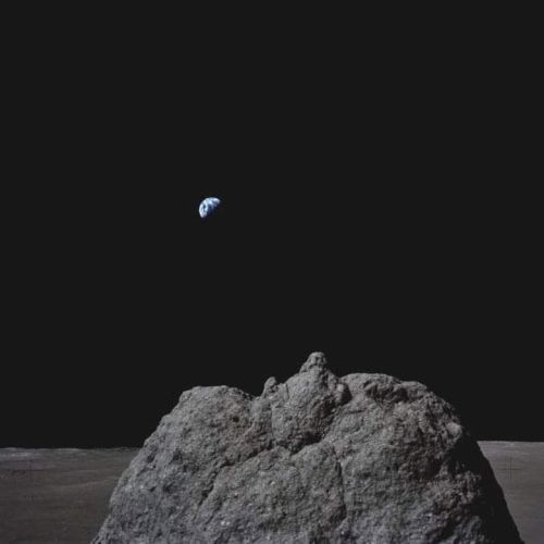 A large rock on the lunar surface with Earth visible in the distant black sky.