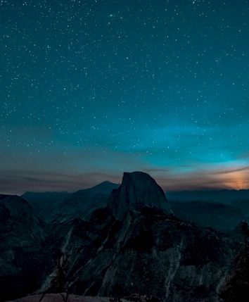 A nighttime landscape of a silhouetted mountain range under a starry sky with a glowing horizon.
