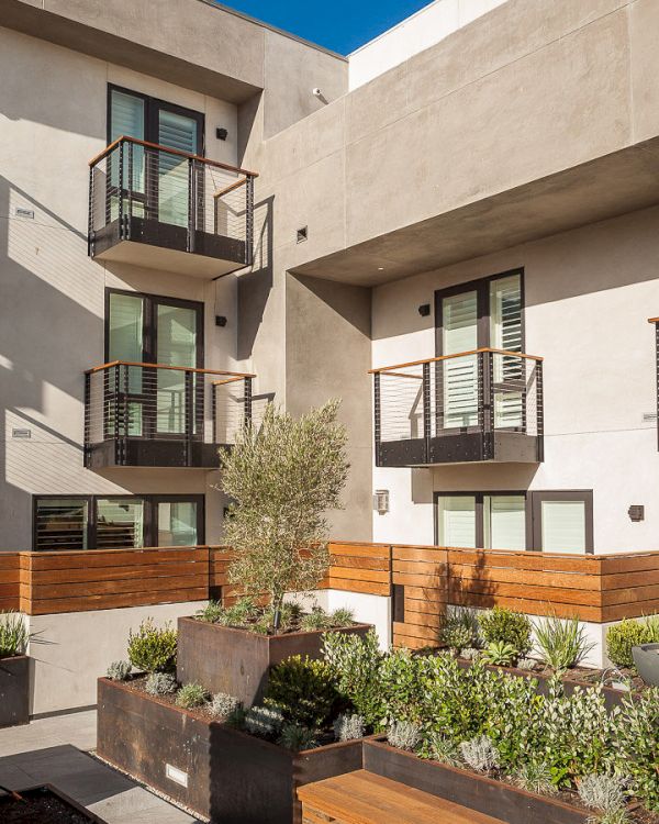 A modern apartment building with balconies and a courtyard featuring planters filled with green plants and shrubs.