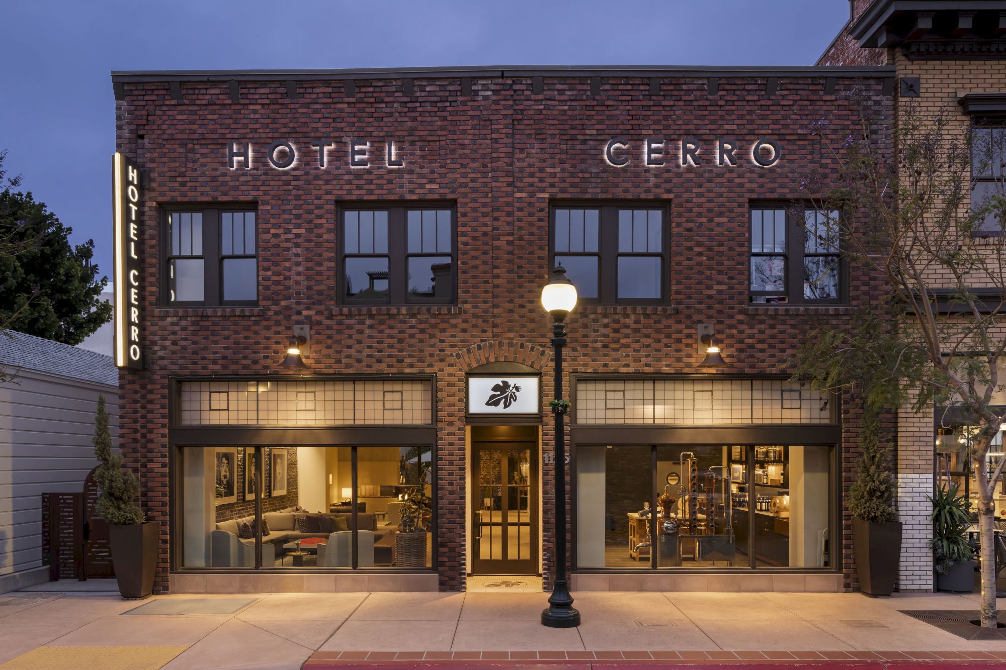The image shows a brick building with the signage "HOTEL CERRO" and a lit street lamp in front, with large windows and doors.