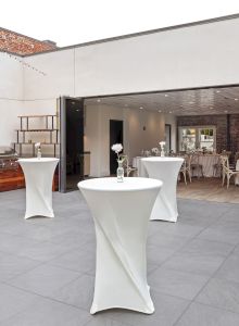Outdoor and indoor event space with cocktail tables, a barbecue grill, and string lights, featuring elegant decor and dining setup.