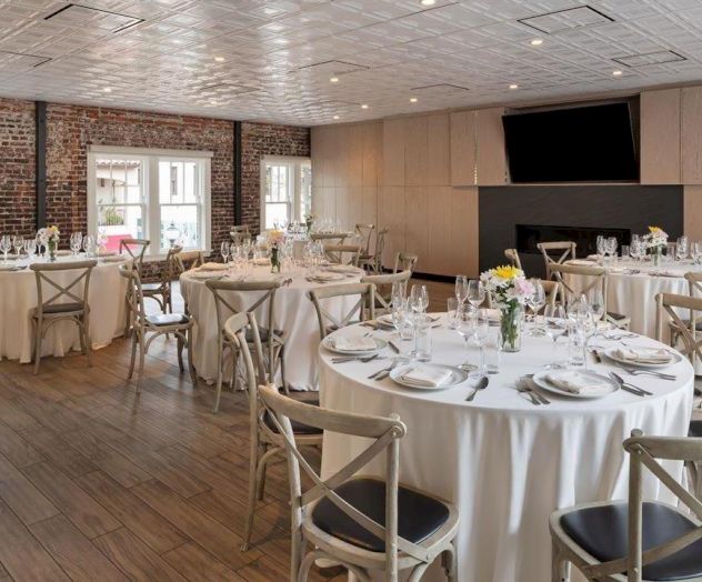 A decorated dining room with round tables set for an event, featuring white tablecloths, elegant tableware, and floral centerpieces.