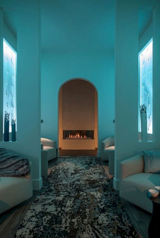 A serene lounge with ambient blue lighting, comfortable seating, decorative vases, and a central fireplace, creating a cozy atmosphere.