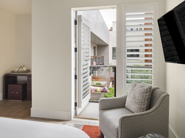 A modern room with a gray chair, wall-mounted TV, and an open door leading to a balcony with garden views outside.