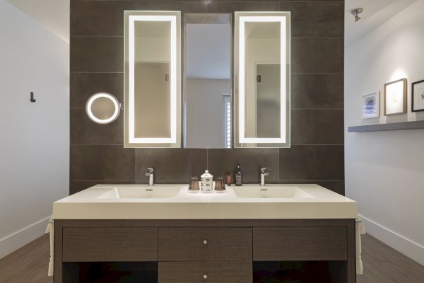 Modern bathroom with double sink, illuminated mirrors, and organized toiletries on the countertop.