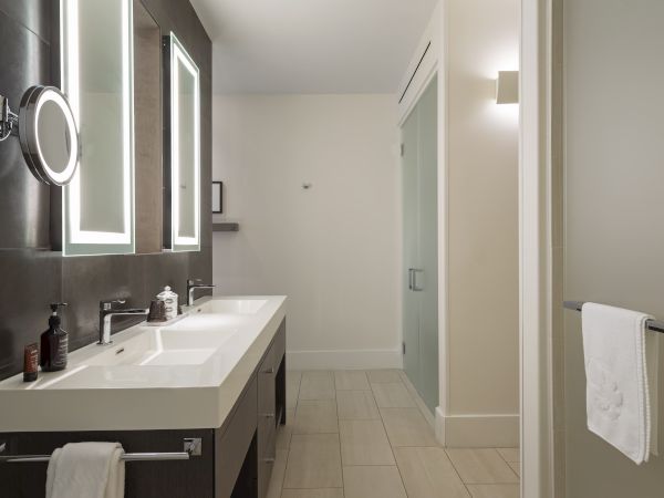 A modern bathroom features a double sink vanity, backlit mirrors, and a towel hanging by the shower area.