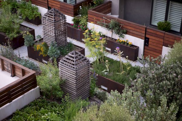 The image shows a rooftop garden with raised wooden planters, lush greenery, herbs, flowers, and wooden lattice structures.