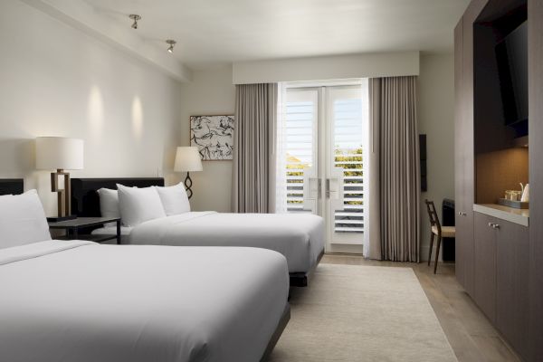 A modern hotel room with two beds, a lamp, artwork, and a window with curtains. A TV and furniture are also visible in the room.