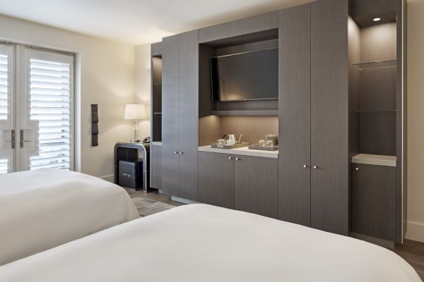 Hotel room with two beds, built-in cabinets, a TV, a lamp, and a door with shutters.