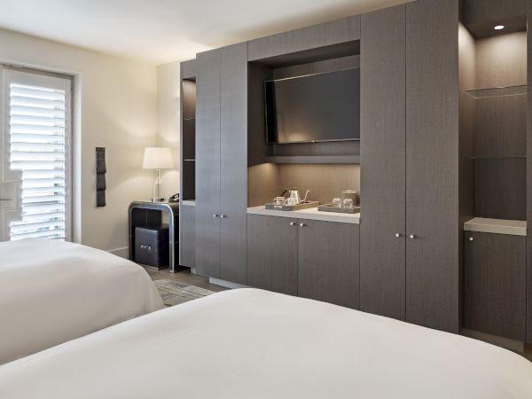 Hotel room with two beds, built-in cabinets, a TV, a lamp, and a door with shutters.