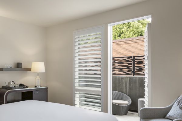 A modern room with a bed, lamp, and a small table with a kettle. It's connected to an outdoor area with a chair and decorative fence.