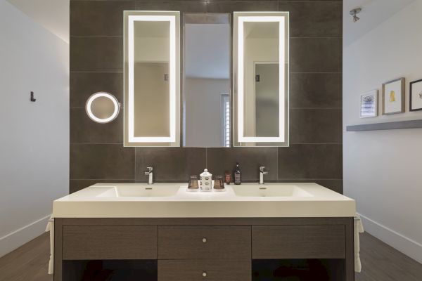 A modern bathroom with double sinks, illuminated mirrors, and a countertop with toiletries.