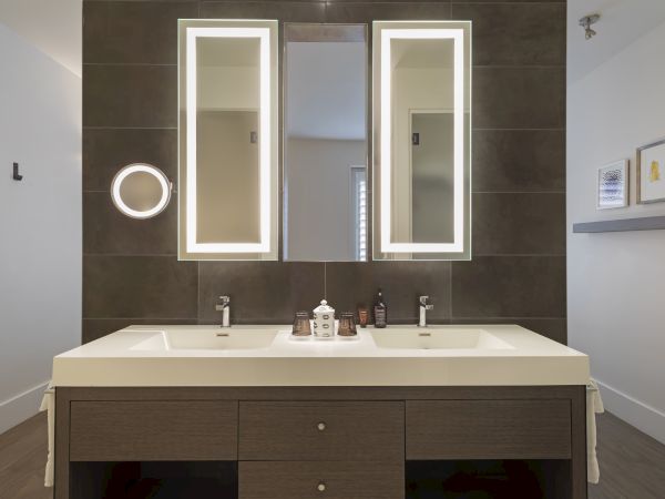 A modern bathroom with double sinks, illuminated mirrors, and a countertop with toiletries.