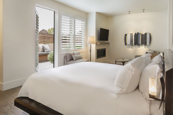 A modern bedroom with a large bed, wall art, TV, and an open door leading to a patio area with seating.