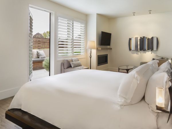 A modern bedroom with a large bed, wall art, TV, and an open door leading to a patio area with seating.