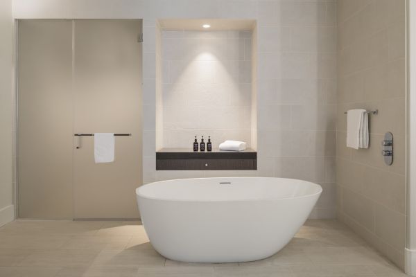 A modern bathroom features a freestanding tub, glass shower door, towels, and toiletries on a shelf under soft lighting.