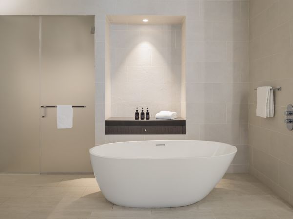 A modern bathroom features a freestanding tub, glass shower door, towels, and toiletries on a shelf under soft lighting.