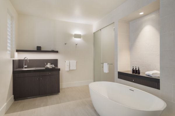 A modern bathroom with a freestanding tub, dark wood cabinets, a sink, towels, and toiletries, lit by soft overhead lighting.