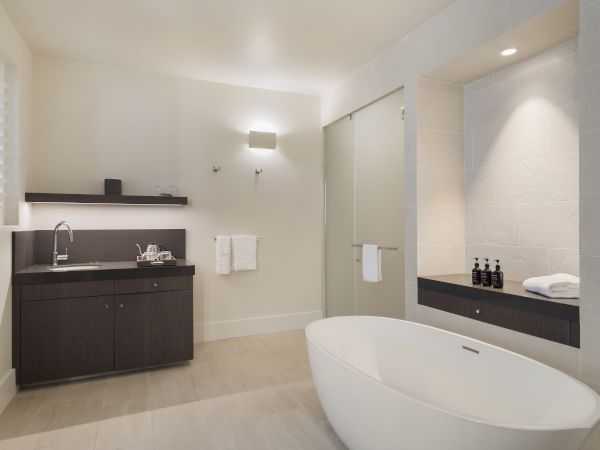 A modern bathroom with a freestanding tub, dark wood cabinets, a sink, towels, and toiletries, lit by soft overhead lighting.