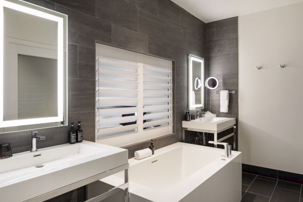 Modern bathroom with a bathtub, two illuminated mirrors, black tiled walls, and a sink with toiletries.