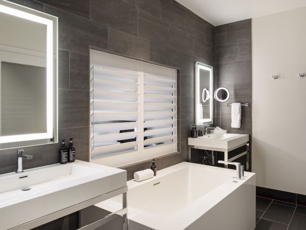 Modern bathroom with a bathtub, two illuminated mirrors, black tiled walls, and a sink with toiletries.