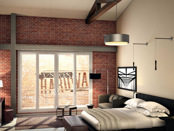 A modern bedroom features exposed brick, a large bed, a sofa, and a wall mirror, with sliding glass doors letting in natural light.