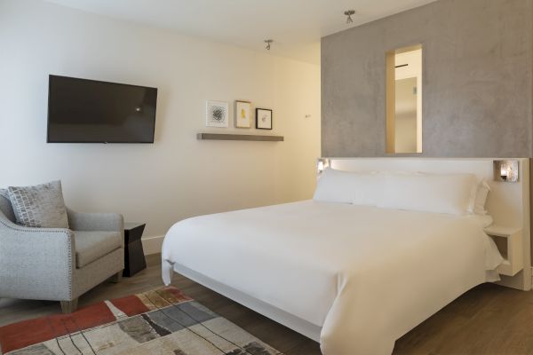 A modern bedroom with a bed, gray chair, wall-mounted TV, and abstract art on the wall.