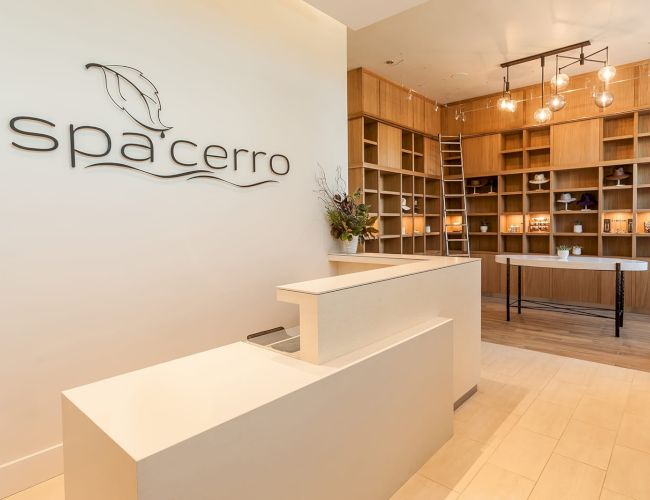 A spa reception area with a modern desk, decorative shelving, lighting, and a sign reading "spa cerro."