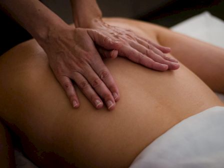 A person receiving a back massage, with two hands applying pressure on the back.
