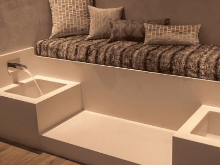 A modern relaxation area with a cushioned seat, geometric pillows, and built-in basins, creating a minimalist yet cozy ambiance.