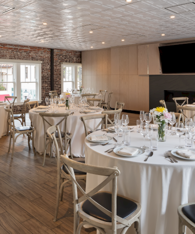 An elegantly set dining room with round tables, white linens, and simple floral centerpieces, suitable for events or gatherings.