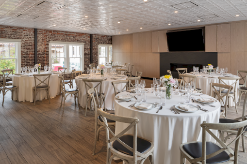 An elegantly set dining room with round tables, white linens, and simple floral centerpieces, suitable for events or gatherings.