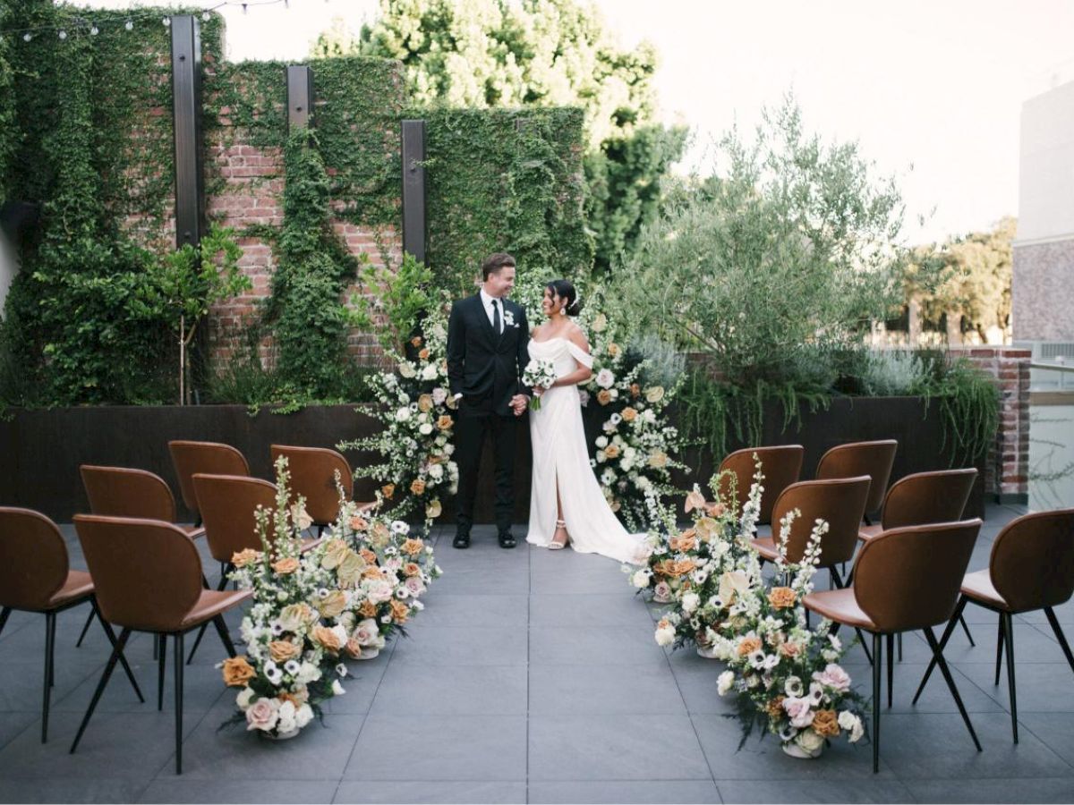 A couple stands in a beautifully decorated outdoor wedding setting with floral arrangements and seating.