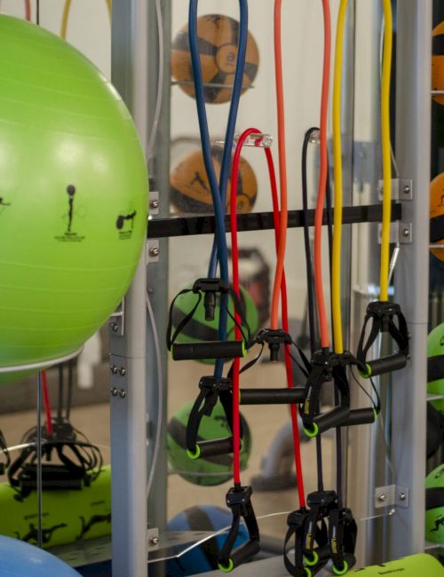 A gym setup featuring exercise balls, resistance bands, and medicine balls organized on a rack.
