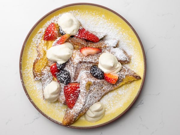 French toast with whipped cream, strawberries, blackberries, and powdered sugar on a yellow plate.