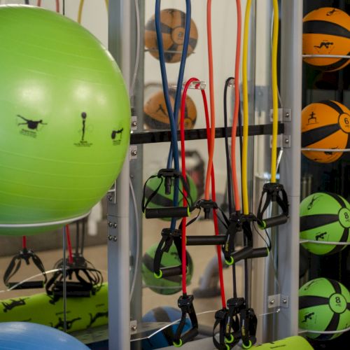The image shows a gym setup with a green exercise ball, resistance bands, and medicine balls on a rack.
