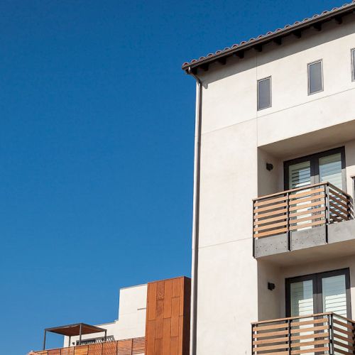 The image shows a modern building with wooden balconies against a clear blue sky.