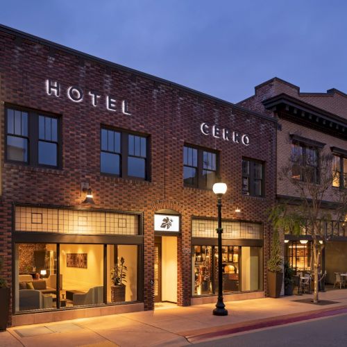 The image shows a street view of Hotel Cerro, a brick building with a lit sign, large windows, and a glowing streetlamp in front.
