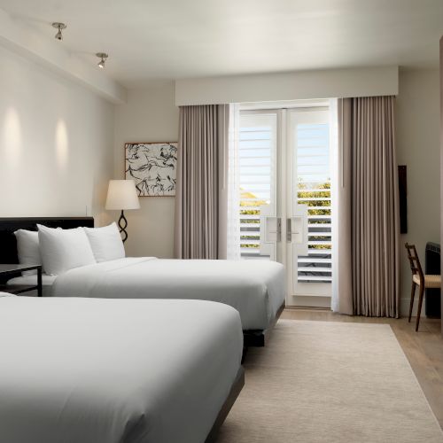 A modern hotel room features two beds, nightstands with lamps, a desk, closet, and access to a balcony through sliding glass doors.
