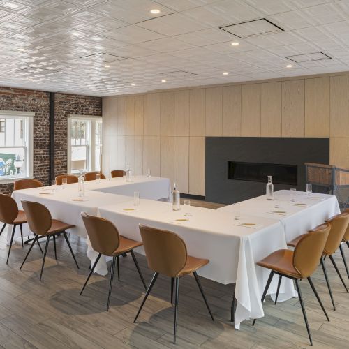 A modern conference room with a U-shaped table setup, brown chairs, water bottles, glasses, and natural light from large windows.