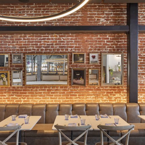 This image shows a restaurant interior with exposed brick walls, decorated mirrors, and tables set with napkins and glasses.
