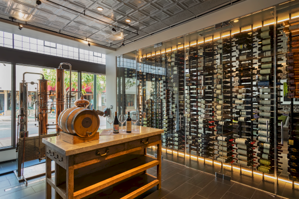 A sophisticated wine storage room features a wooden barrel, wine bottles, glasses, and a display of wine racks against a glass wall.