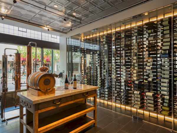 A sophisticated wine storage room features a wooden barrel, wine bottles, glasses, and a display of wine racks against a glass wall.