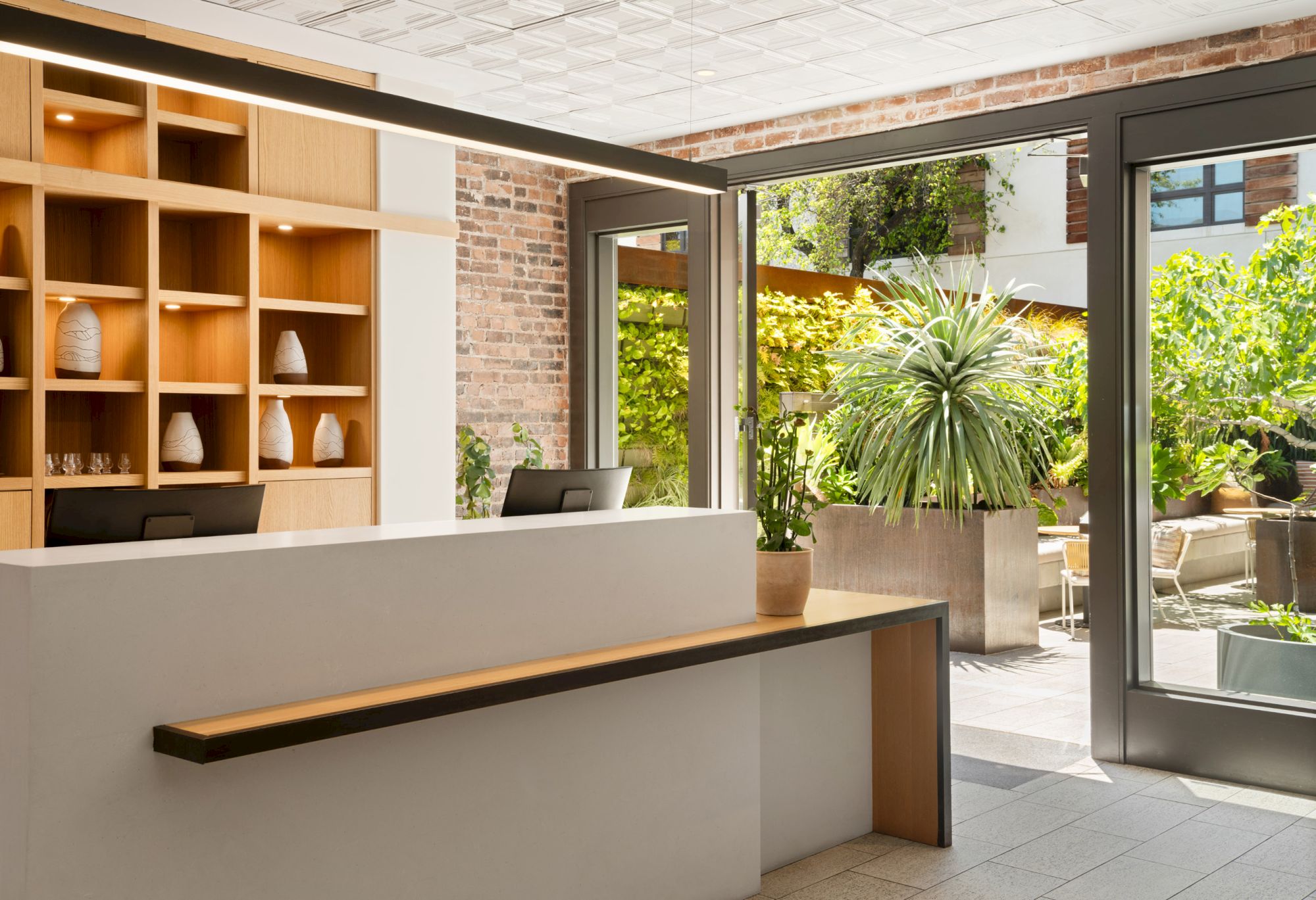 The image shows a modern reception area with a desk, wooden shelves, and large windows overlooking a garden.
