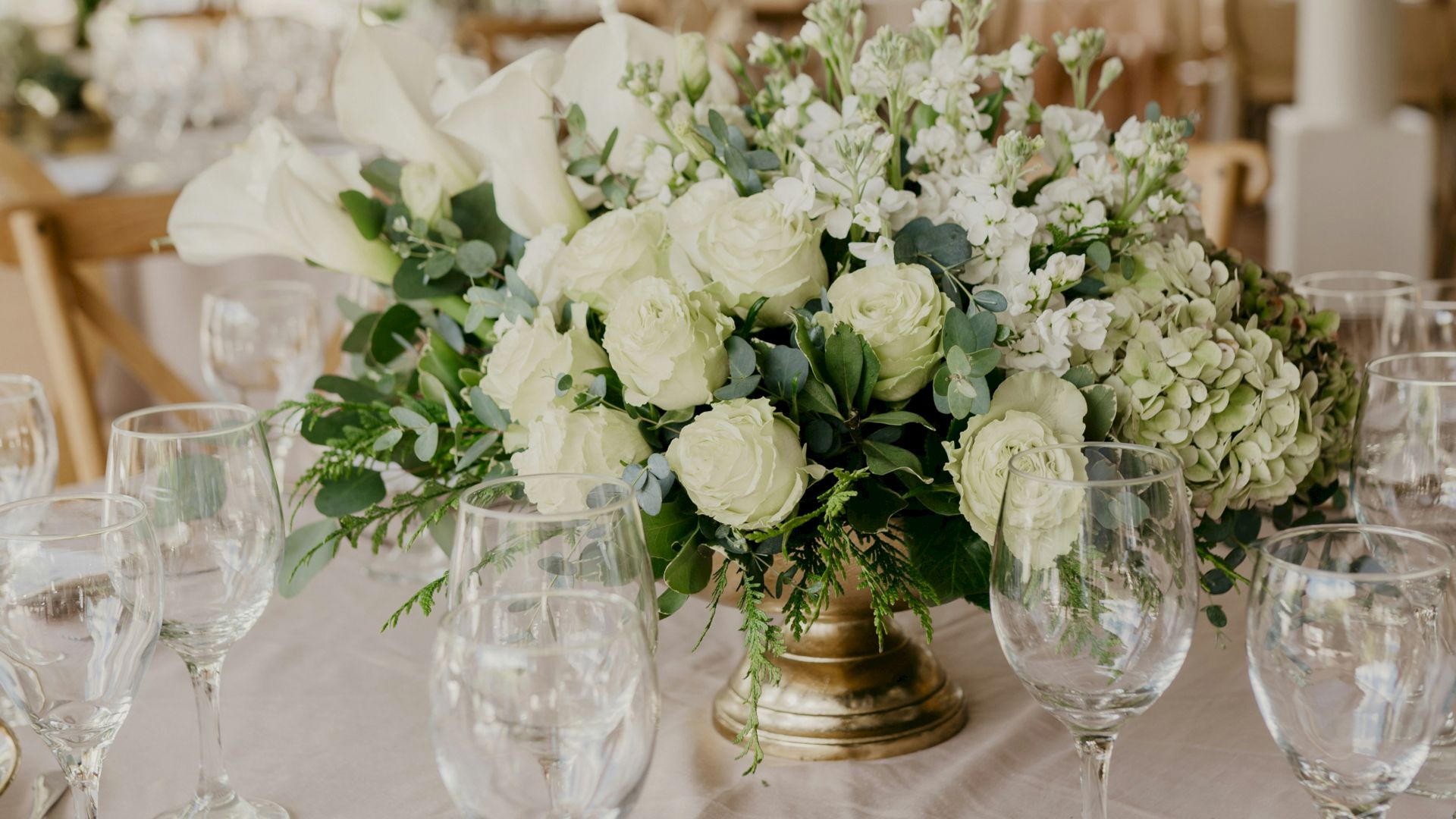 A beautifully set table with elegant floral centerpiece, glassware, cutlery, and menus in a softly lit, possibly outdoor event setting.